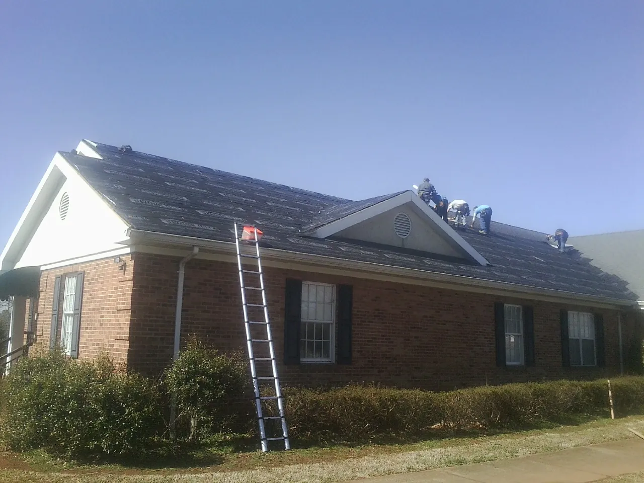 Crew tearing shingles off a brick ranch roof with a ladder set — Emergency Roof Repair work by our crew in Champaign
