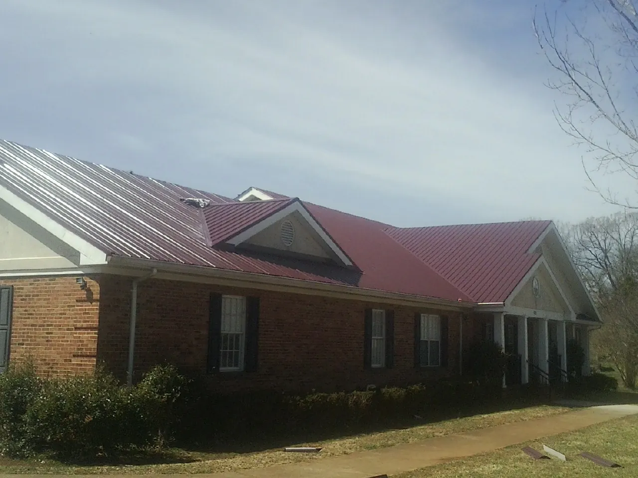 Red metal roof with gabled entries on a long brick building, from a Hail Damage Roof Repair job in Champaign