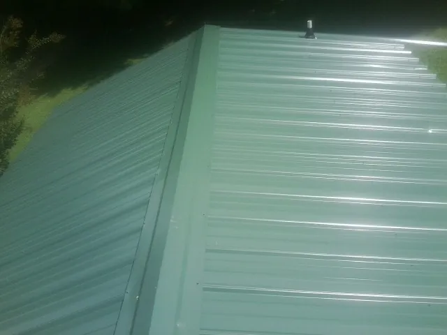 New green metal panels meeting at the ridge of a roof — Flat Roof Repair work by our crew in Champaign