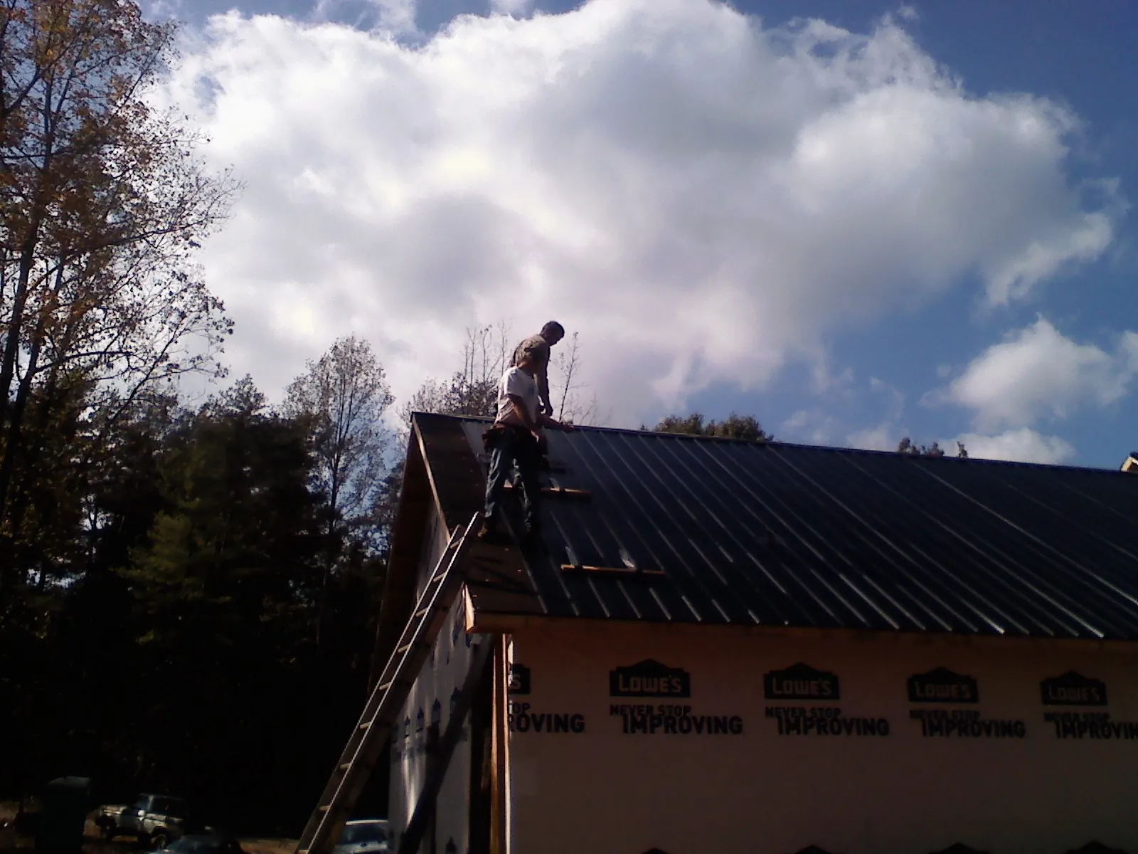 Roofer fastening dark metal panels high against a cloudy sky, from a Roof Inspection job in Champaign