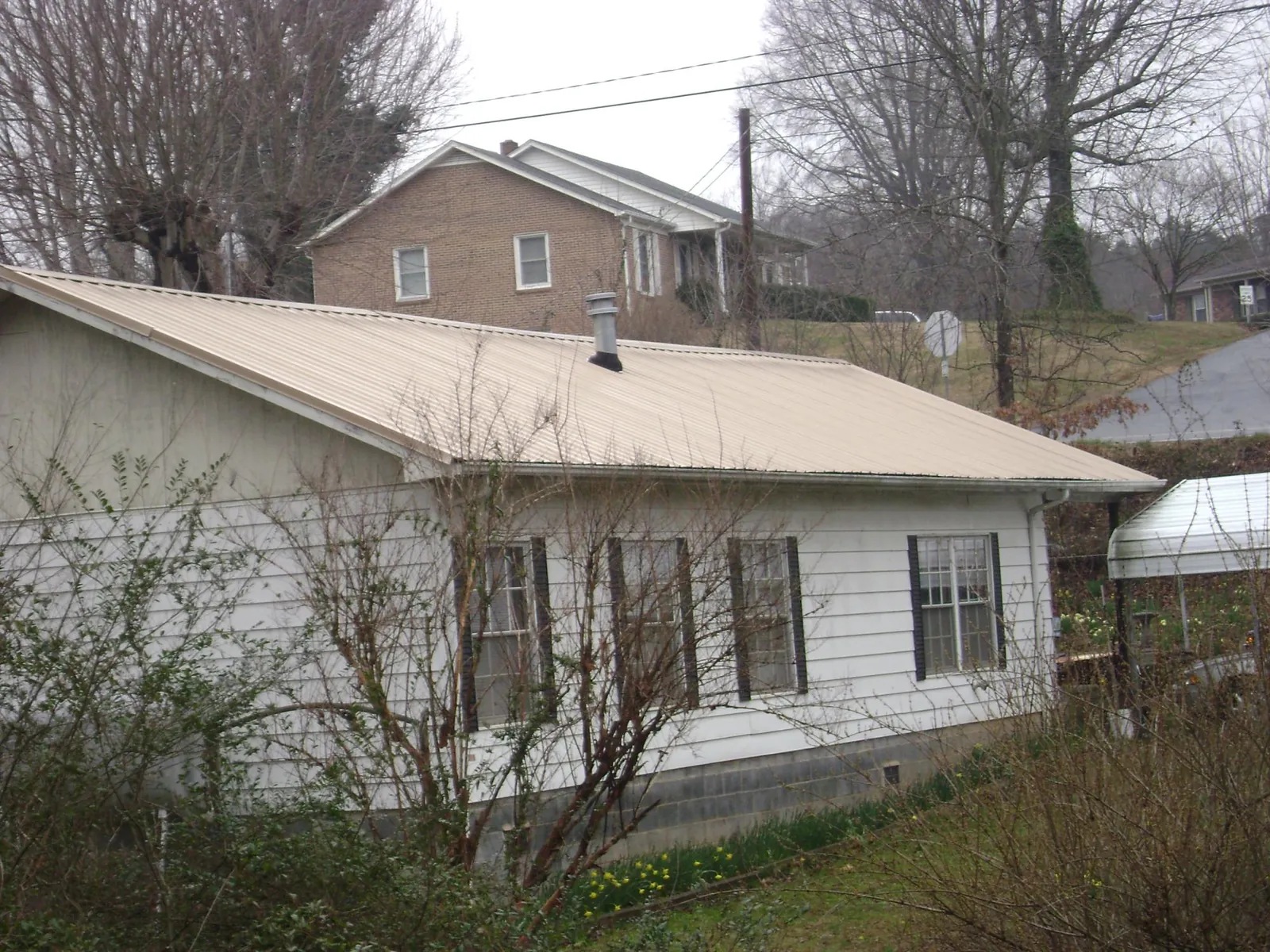 Tan metal roof on a white sided house set into a hillside — Commercial Roofing by Roofing Brothers in Champaign
