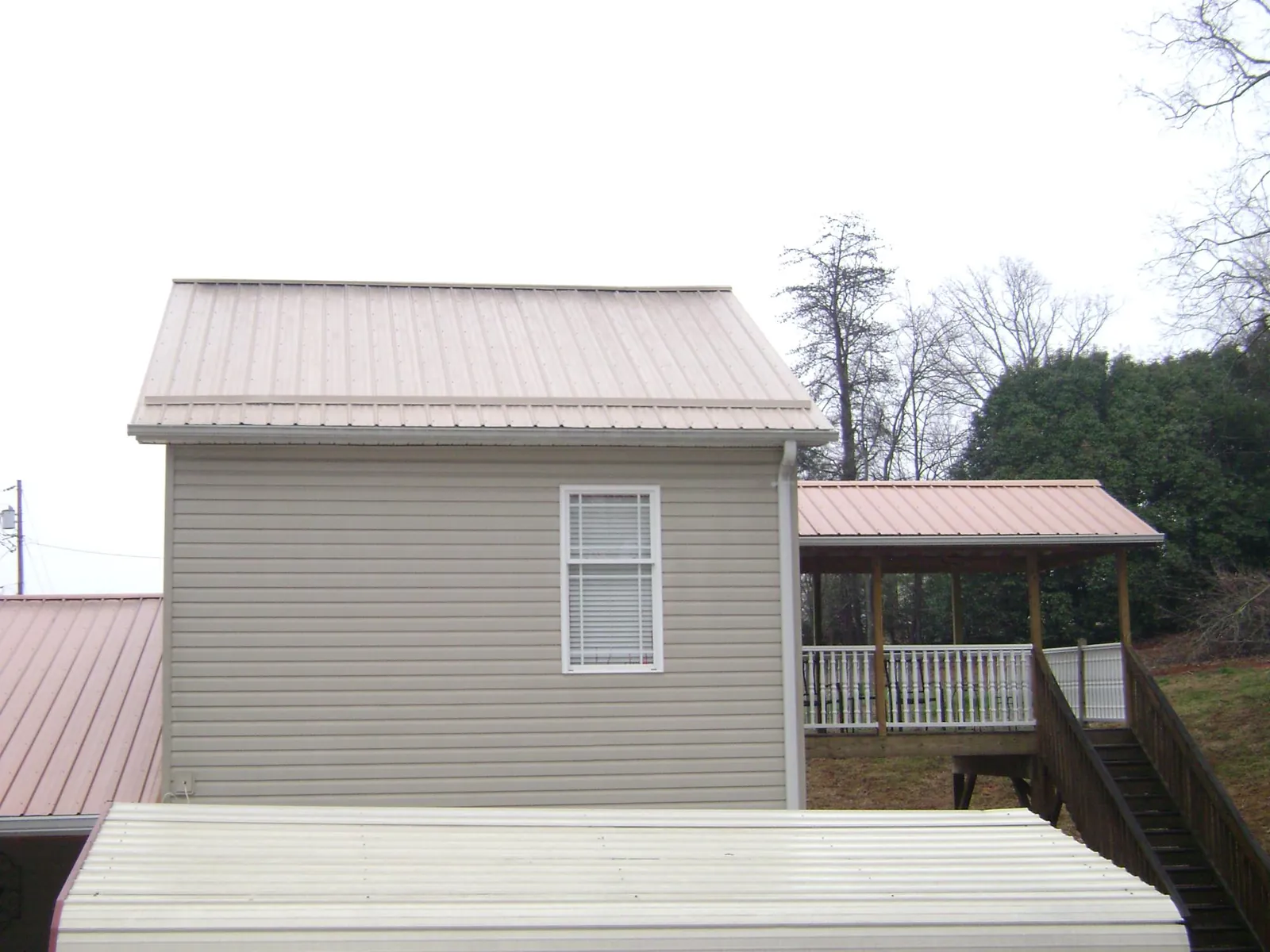 Tan metal roofs on a two story addition and attached porch, from a Roof Replacement job in Champaign